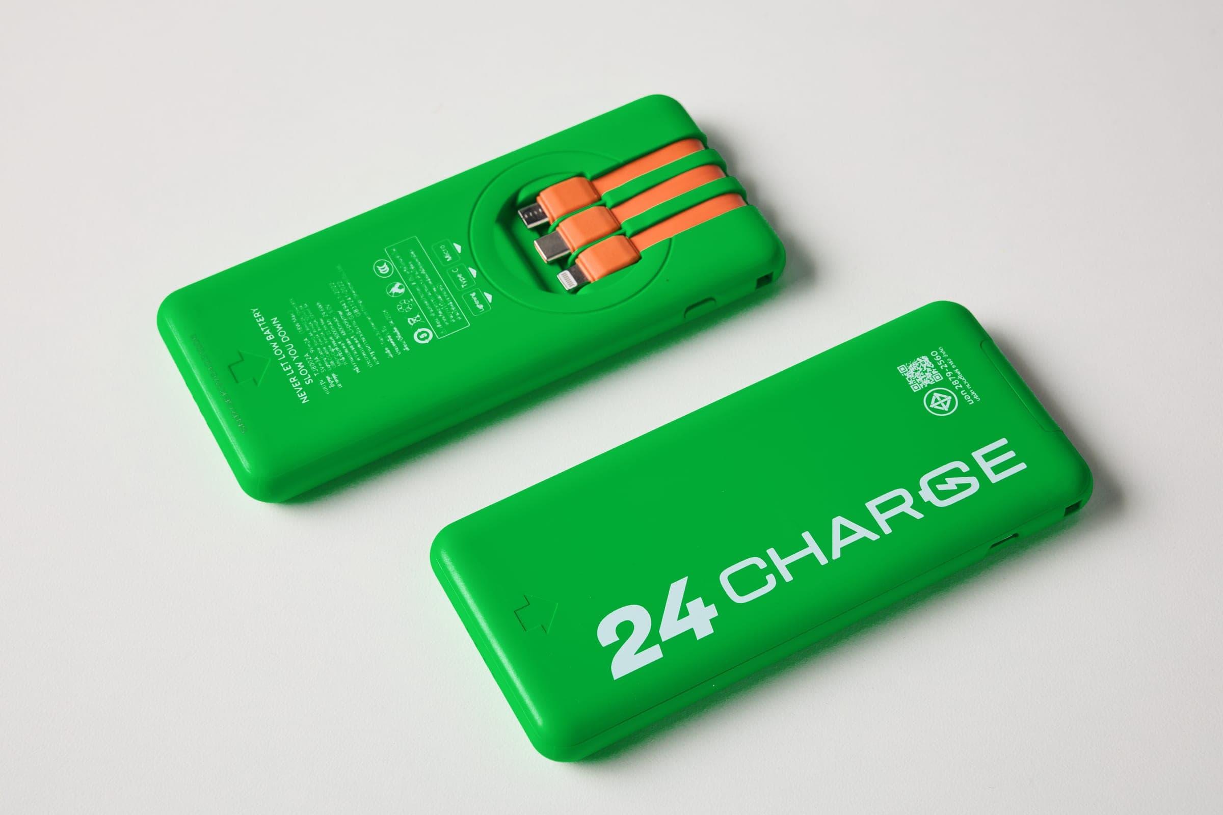 พาวเวอร์แบงก์ 24CHARGE มุมมองที่ 3 ด้านหลังตัวเครื่องตั้งขึ้น ดึงสายชาร์จในตัวสีส้มทั้งสามหัว (Lightning, Type-C, Micro) ออกมา พร้อมข้อความสเปกและคำเตือนพิมพ์อยู่บนตัวเครื่อง