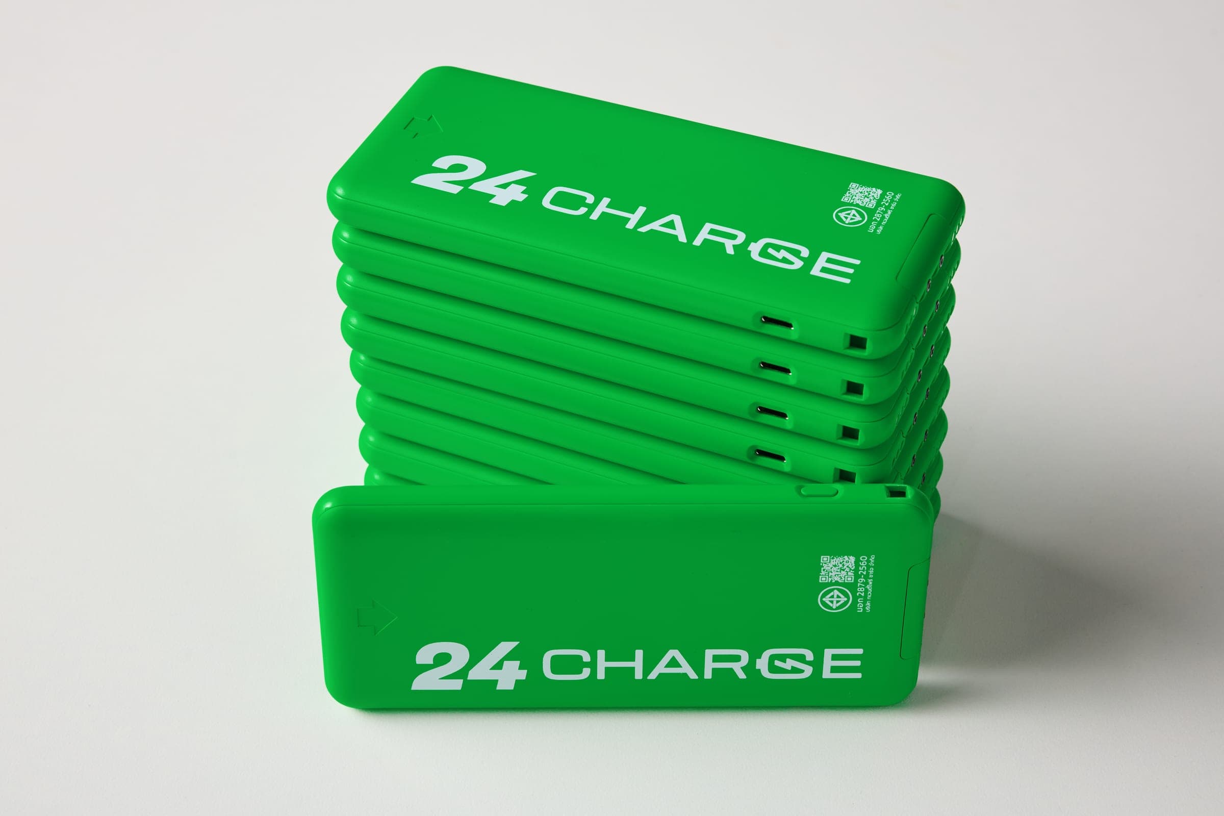 พาวเวอร์แบงก์ 24CHARGE มุมมองที่ 4 สองตัววางเรียงเฉียงคู่กัน ตัวด้านหลังเผยสายชาร์จในตัวสามหัวที่ดึงออก ส่วนตัวด้านหน้าคว่ำเห็นโลโก้ 24CHARGE
